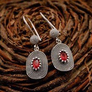 May include: A pair of silver earrings with red gemstone accents. The earrings feature a delicate, twisted design and a small, round bead at the top.