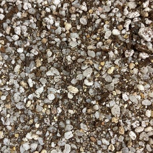 Peut inclure: Gros plan d'un mélange de terre et de petits galets clairs. Les galets varient en taille et en forme, certains apparaissant translucides. La terre est de couleur brun foncé et la texture générale est grossière et granuleuse.