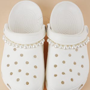 May include: White clogs with a pearl trim around the top of the shoe.