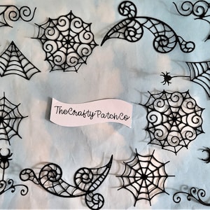 May include: A set of 10 black paper die-cut spiderweb designs, including corner pieces, swirls, and a full spiderweb. The designs are perfect for Halloween crafts and decorations.