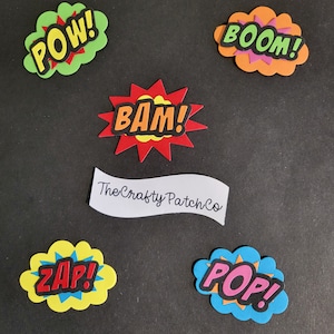 Può includere: Cinque sagome di schiuma colorate di effetti sonori dei fumetti. Le parole sono "POW!" in verde, "BOOM!" in arancione, "BAM!" in rosso, "ZAP!" in giallo e "POP!" in blu. Le parole sono in grassetto, in nero. Le sagome sono su uno sfondo nero. Il testo "The Crafty Patch Co" è su uno striscione bianco.