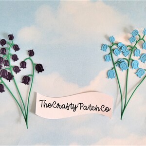 May include: Two metal flower clusters, one purple and one light blue, with green stems. The purple flowers are bell-shaped. The light blue flowers are also bell-shaped. The text "The Crafty Patch Co" is on a white banner.