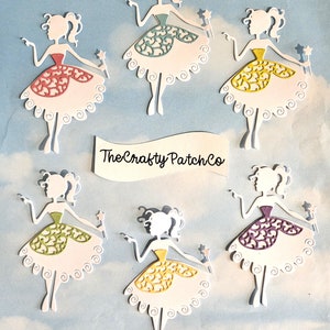 May include: Six white die-cut paper fairy silhouettes with different coloured dresses. The fairies are holding a star wand in their right hand and have a curly hairstyle. The dresses are teal, yellow, red, green, purple, and yellow. The text "The Crafty Patch Co." is on a white banner.