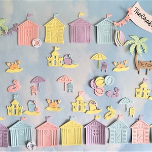 Puede incluir: Una colección de troqueles con temática de playa en colores pastel. Incluye cabañas de playa, castillos de arena, palmeras, cangrejos, sombrillas y salvavidas. El texto "The Crafty Patch Co." está en una pancarta.