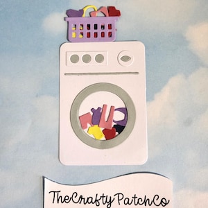 May include: A white washing machine with a purple laundry basket on top, filled with colourful clothes. The washing machine's door reveals more clothes inside. The text "The Crafty Patch Co" is displayed on a white banner below the machine.