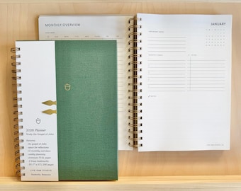 May include: A green 2026 planner with gold spiral binding and a white spine. The planner includes a monthly overview and a January calendar page. The cover features an acorn design and the text "2026 Planner".