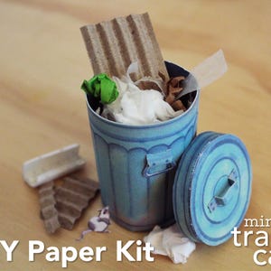 May include: A blue paper mini trash can with a matching lid, featuring a DIY paper kit design. The container is filled with small scraps of brown corrugated cardboard, white paper, and a green paper ball, with a small paper mouse cutout nearby.