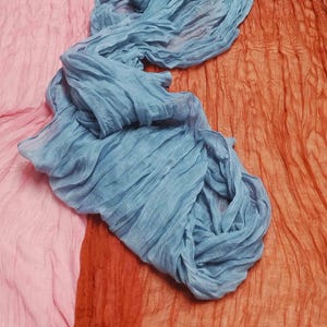 Könnte beinhalten: Nahaufnahme von drei Stoffen in Rosa, Blau und Orange. Der blaue Stoff ist über dem orangefarbenen Stoff drapiert. Der rosa Stoff befindet sich links. Die Stoffe haben eine gekräuselte Textur.