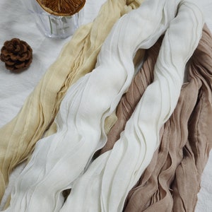 May include: Three fabric scarves in beige, white and brown. The scarves are made of a soft, crinkled fabric and are arranged in a pile.