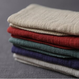 May include: A stack of five fabric squares in different colors. The top square is beige, the second is red, the third is green, the fourth is dark blue, and the bottom square is beige.