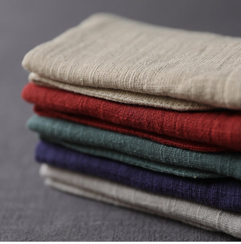 May include: A stack of five fabric squares in different colors. The top square is beige, the second is red, the third is green, the fourth is dark blue, and the bottom square is beige.