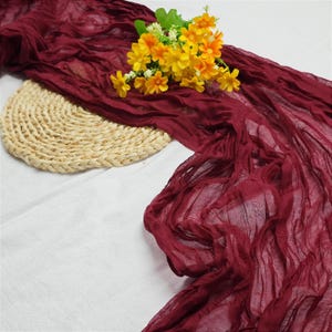May include: A deep red sheer fabric draped over a woven straw placemat with a bouquet of yellow flowers on top.