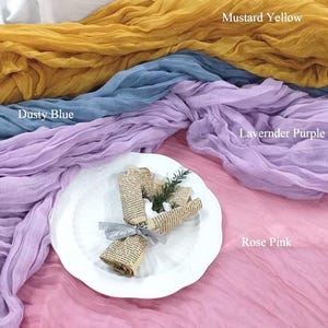May include: A photograph showcasing fabric swatches in mustard yellow, dusty blue, lavender purple, and rose pink. A white plate displays a small bouquet wrapped in vintage paper and tied with a grey ribbon. The text "Mustard Yellow", "Dusty Blue", "Lavender Purple", and "Rose Pink" are visible.