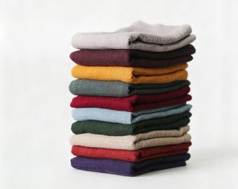 May include: A vertical stack of twelve folded fabric napkins in various solid colors including light gray, dark maroon, mustard yellow, sage green, bright red, light blue, forest green, beige, crimson, and deep purple with a visible woven texture.
