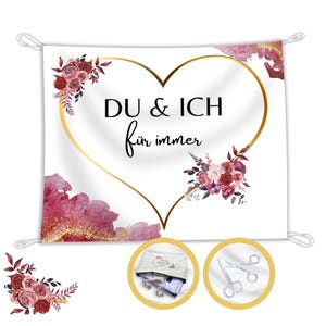 Könnte beinhalten: Weißes Banner mit goldenem Herzumriss und dem Text "DU & ICH für immer". Das Banner ist mit burgunderroten und rosa Blumenarrangements und Aquarellakzenten verziert. Enthält einen kleinen Beutel und eine Schere.