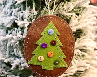 Può includere: Un ornamento natalizio in feltro marrone a forma di albero con foglie in feltro verde e bottoni colorati.