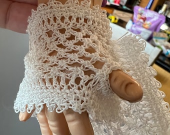 May include: White crocheted lace wristlet with a delicate pattern. The wristlet is made of a fine, lightweight yarn and has a scalloped edge.