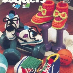 May include: A pattern booklet titled Little Joggers Crochet featuring instructions for handmade baby shoes. The cover displays crocheted trainers in white, purple, and blue, orange and pink booties with bows, and red, green, and blue high-top trainers.