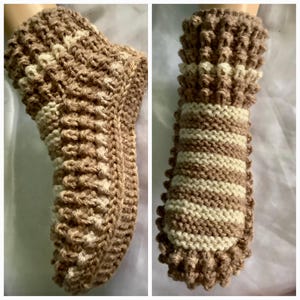 Puede incluir: Un par de calcetines de pantuflas de punto marrón y blanco. Los calcetines tienen un patrón texturizado y están hechos con un hilo suave.