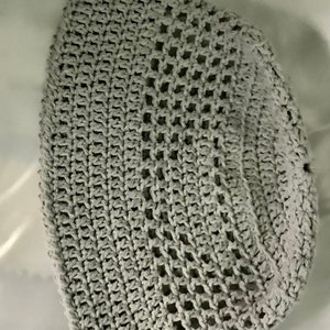 Pu&ograve; includere: Un cappello a secchiello in crochet grigio con un design a rete.