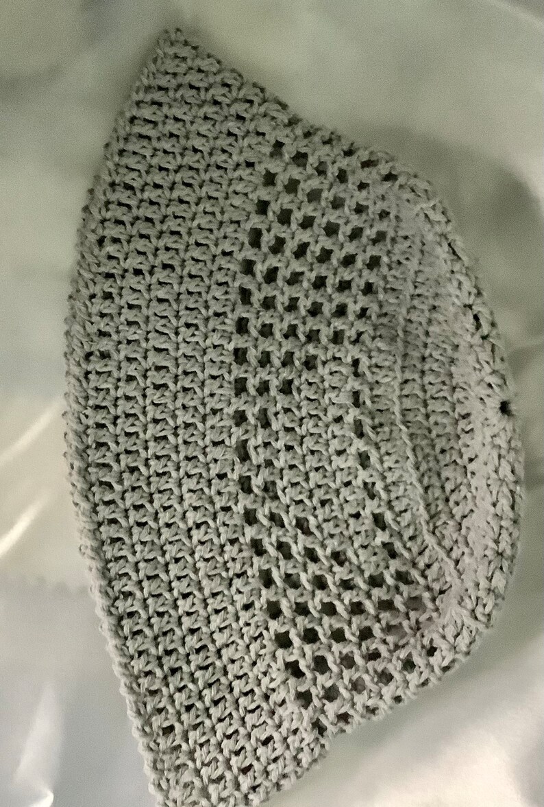 Pu&ograve; includere: Un cappello a secchiello in crochet grigio con un design a rete.