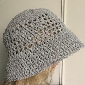 Pu&ograve; includere: Un cappello a secchiello in crochet grigio con un'ampia tesa e un motivo a maglia aperta.