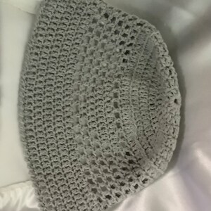 Pu&ograve; includere: Un cappello da sole in crochet grigio con un'ampia tesa e un motivo a trama aperta.