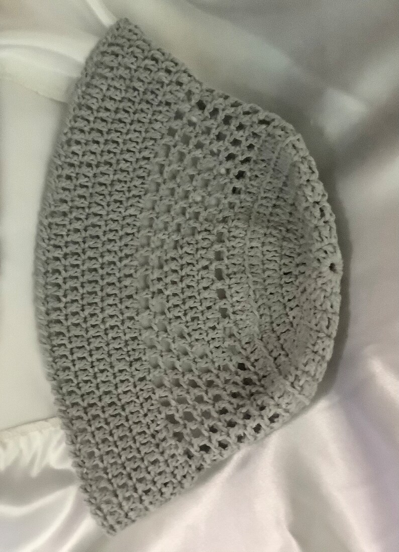 Pu&ograve; includere: Un cappello da sole in crochet grigio con un'ampia tesa e un motivo a trama aperta.