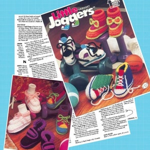 May include: A pattern booklet titled Little Joggers by Annie's Attic featuring instructions and photographs of various crocheted baby shoes. The images display colourful yarn footwear in styles resembling trainers and boots, arranged with small dumbbells.