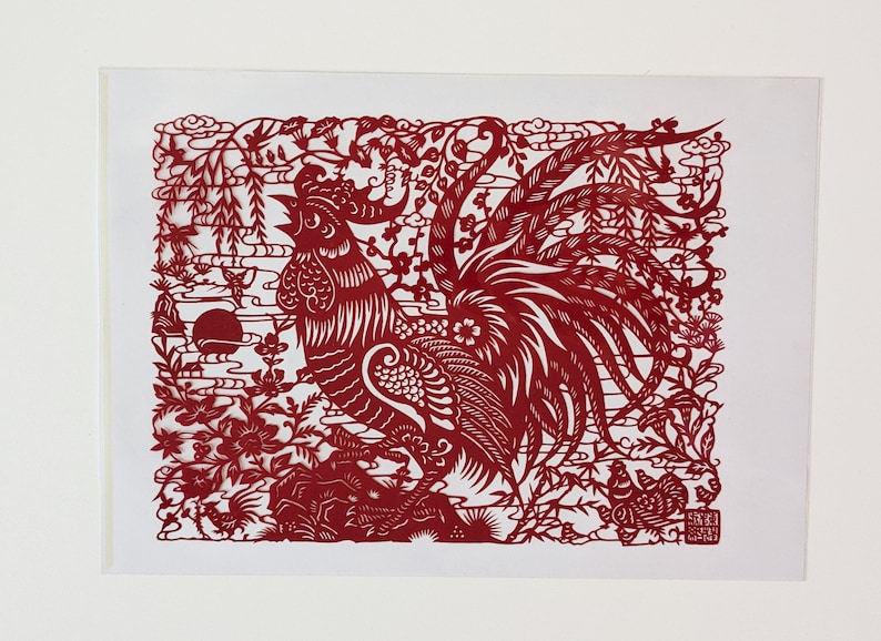 May include: Red paper cut-out art depicting a rooster with intricate details. The rooster is surrounded by flowers, clouds, and bamboo.