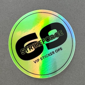 Könnte beinhalten: Ein runder holografischer Aufkleber mit dem Text "STRIKE FORCE" und "VIP STICKER OPS" in Schwarz. Der Aufkleber hat einen grün-gelben schillernden Effekt und einen schwarzen Rand.