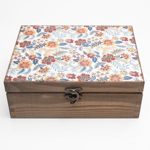 Peut inclure: Une boîte en bois avec un couvercle à motif floral et un loquet en laiton. La boîte est brune et a une finition en bois naturel.