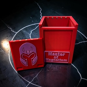 May include: A red rectangular storage container with a detachable lid. The lid features a raised light purple helmet emblem. The front of the container displays a light purple rectangular plaque with the embossed text Master of Magnetism.