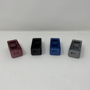 May include: Four small rectangular boxes in different colors: burgundy, black, blue, and gray. The boxes are made of a smooth, textured material.