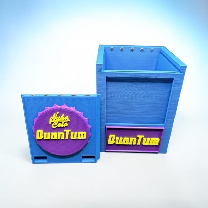 Pu&ograve; includere: Due contenitori blu stampati in 3D. Uno &egrave; rettangolare con un logo Nuka Cola Quantum giallo e viola. L'altro &egrave; un contenitore pi&ugrave; grande, con la parte superiore aperta, con il logo Quantum. Entrambi hanno un'estetica retr&ograve; da videogioco.