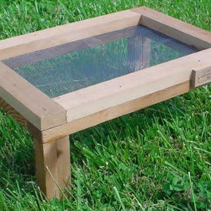 May include: A wooden frame with a mesh screen, sitting on four legs. The frame is made of natural wood and has a rustic look. The mesh screen is made of metal and is designed to keep insects out.