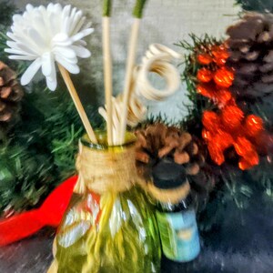 Op de afbeelding: Een heldere glazen diffuserfles met een jutewikkel en een schelpbasis. De fles is gevuld met houten stokjes en witte bloemenaccenten.