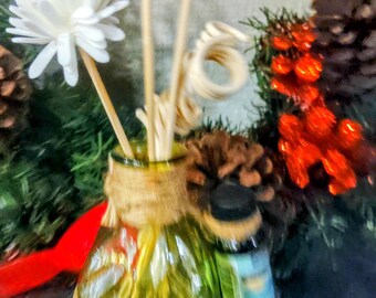 Op de afbeelding: Een heldere glazen diffuserfles met een jutewikkel en een schelpbasis. De fles is gevuld met houten stokjes en witte bloemenaccenten.