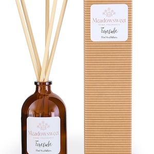 May include: A brown glass bottle with a white label that reads "Meadowsweet Home Fragrance Fireside 100ml Reed Diffuser". The bottle is filled with a clear liquid and has a set of wooden sticks inserted into it. The bottle is sitting on a white surface next to a brown cardboard box with the same label.