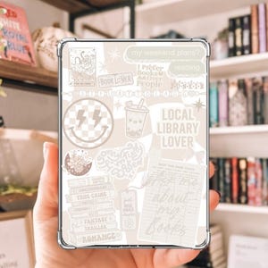 Op de afbeelding: Een doorzichtige telefoonhoes met een beige stickercollage met de tekst "Local Library Lover", "Book Lover" en "I prefer books over people". De collage bevat een smiley met bliksemschichten, een boba-drankje en andere graphics met boeken als thema.