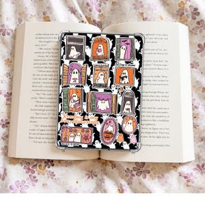May include: A clear phone case featuring a Halloween-themed design. The case showcases various cartoon ghosts in windows, with the text "Reading is my beautiful escape" and "Too Cute to Spook". The design includes orange, purple, and black accents.