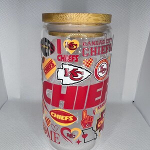 May include: A clear glass jar with a bamboo lid, decorated with red, yellow, and white Kansas City Chiefs logos and graphics. The jar has the words "Chiefs" and "Home is where the Chiefs are" printed on it.