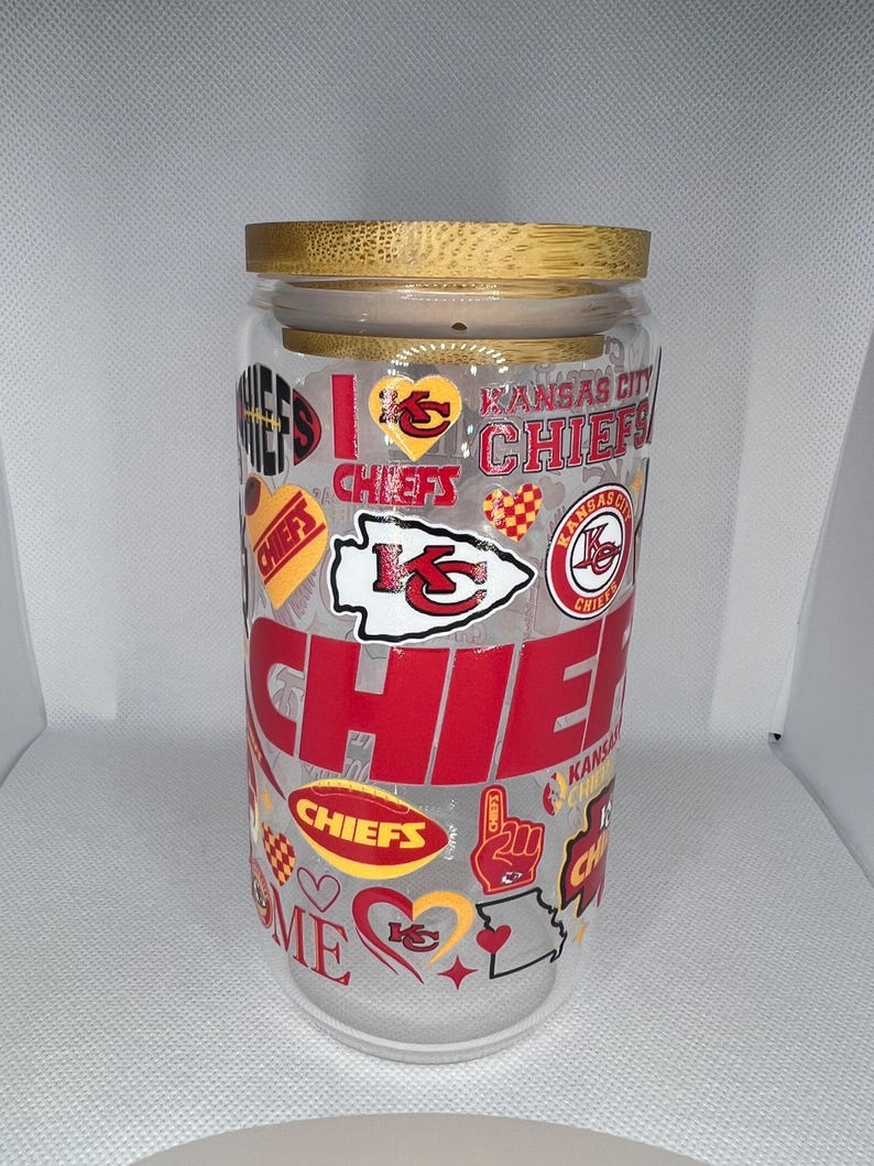 May include: A clear glass jar with a bamboo lid, decorated with red, yellow, and white Kansas City Chiefs logos and graphics. The jar has the words "Chiefs" and "Home is where the Chiefs are" printed on it.
