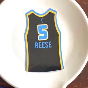 May include: Black basketball jersey with blue trim and a blue number 5 on the back. The name "REESE" is printed below the number.