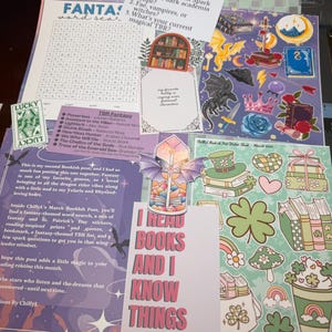 Puede incluir: Una colección de artículos de papelería con temática de fantasía, que incluye pegatinas, un marcapáginas y una sopa de letras. Las pegatinas presentan libros, dragones y temas del Día de San Patricio. El marcapáginas dice "I Read Books and I Know Things."