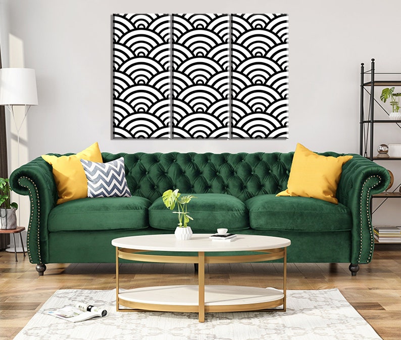 Może przedstawiać: Zielona welurowa sofa z pikowaniem i złotymi gwoździami ozdobnymi. Sofa ma dwa ż&oacute;łte poduszki i jedną poduszkę w szaro-białe wzory. Sofa stoi przed białą ścianą, nad kt&oacute;rą wisi czarno-biały geometryczny wydruk.