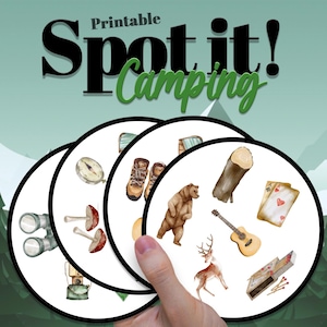 May include: A hand holds three circular cards from a "Spot it! Camping" game. Each card features camping-themed illustrations like a compass, bear, and guitar. The game's title is printed at the top in black and green.