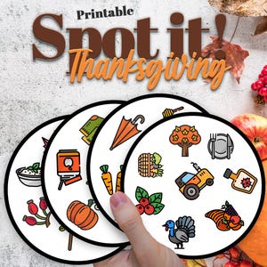 May include: A person holding four circular game cards with Thanksgiving illustrations. The cards show images of a pumpkin, a turkey, a tractor, and other autumn-related items. The words "Printable Spot it! Thanksgiving" are at the top.