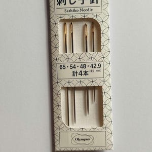 Puede incluir: Un paquete de cuatro agujas de sashiko de ojo dorado en una caja blanca con texto negro que dice "刺し子針 Sashiko Needle 65・54・48・42.9 計4本 (単位:mm) Olympus".