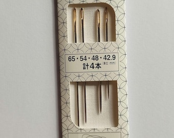 Könnte beinhalten: Eine Packung mit vier Olympus Sashiko-Nadeln in einer cremefarbenen Kartonhülle mit wiederkehrendem geometrischen Muster. Die Verpackung zeigt den Text Sashiko Needle, 65, 54, 48, 42.9 und gibt eine Gesamtzahl von 4 Nadeln in Millimetern an.